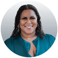 Brittney has long black curly hair, dark skin, and is wearing a teal blouse.