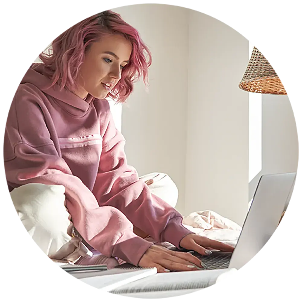 A female teenager with short pink hair studying on a laptop in her bedroom. A female teenager with short pink hair studying on a laptop in her bedroom.